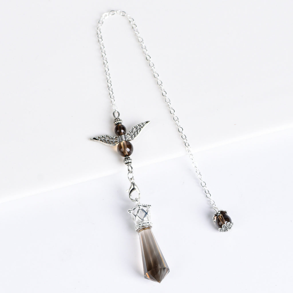 Angel-wing crystal pendulum held by its chain during a simple personal ritual setting
