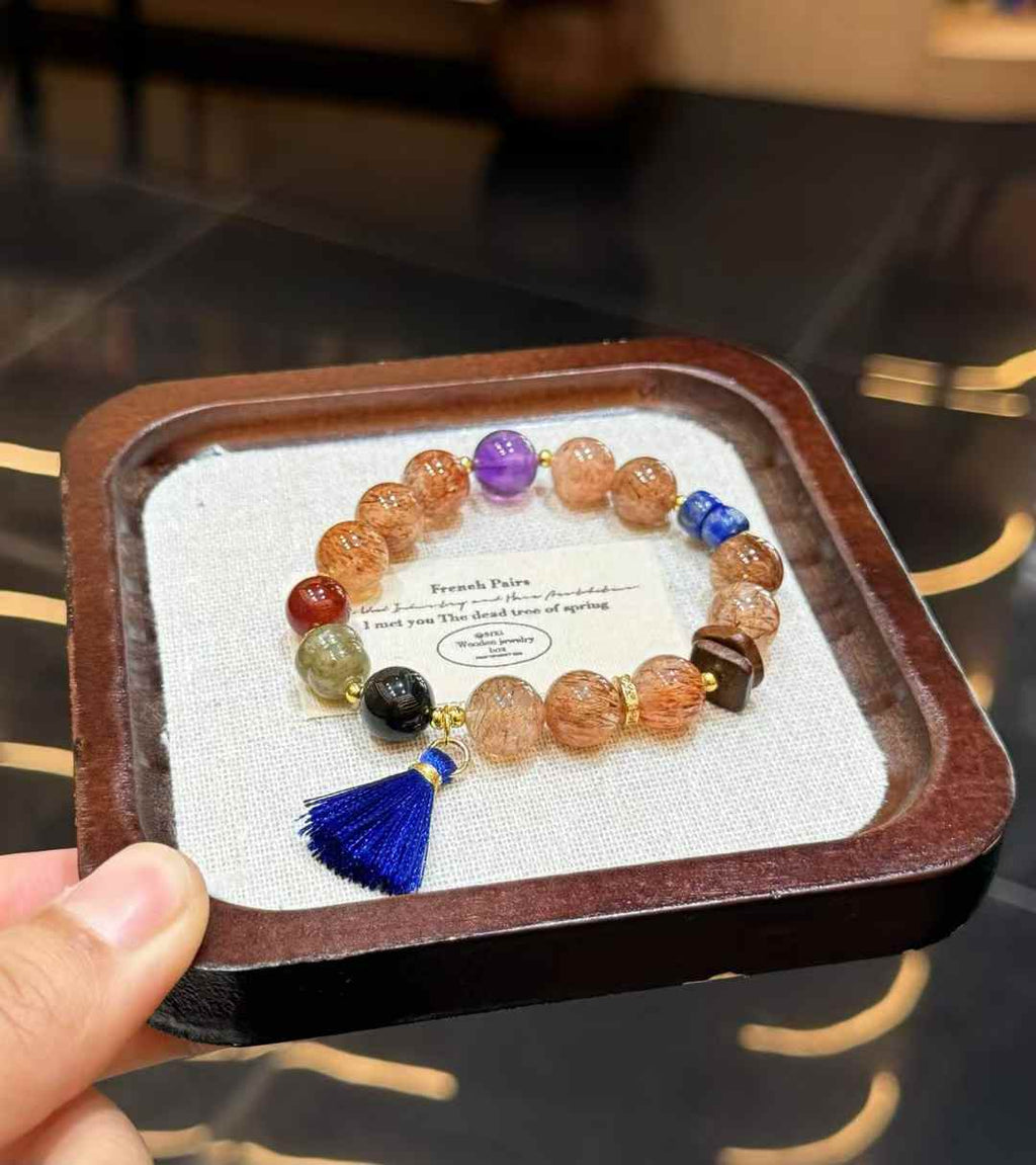 Veridia Black Gold Super Seven mixed gemstone bracelet with blue tassel displayed on a jewelry tray