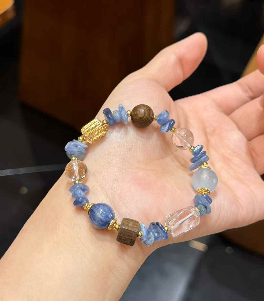Handheld view of the Blue Crystal, Aquamarine and Clear Quartz bracelet with wood and gold-tone accent details