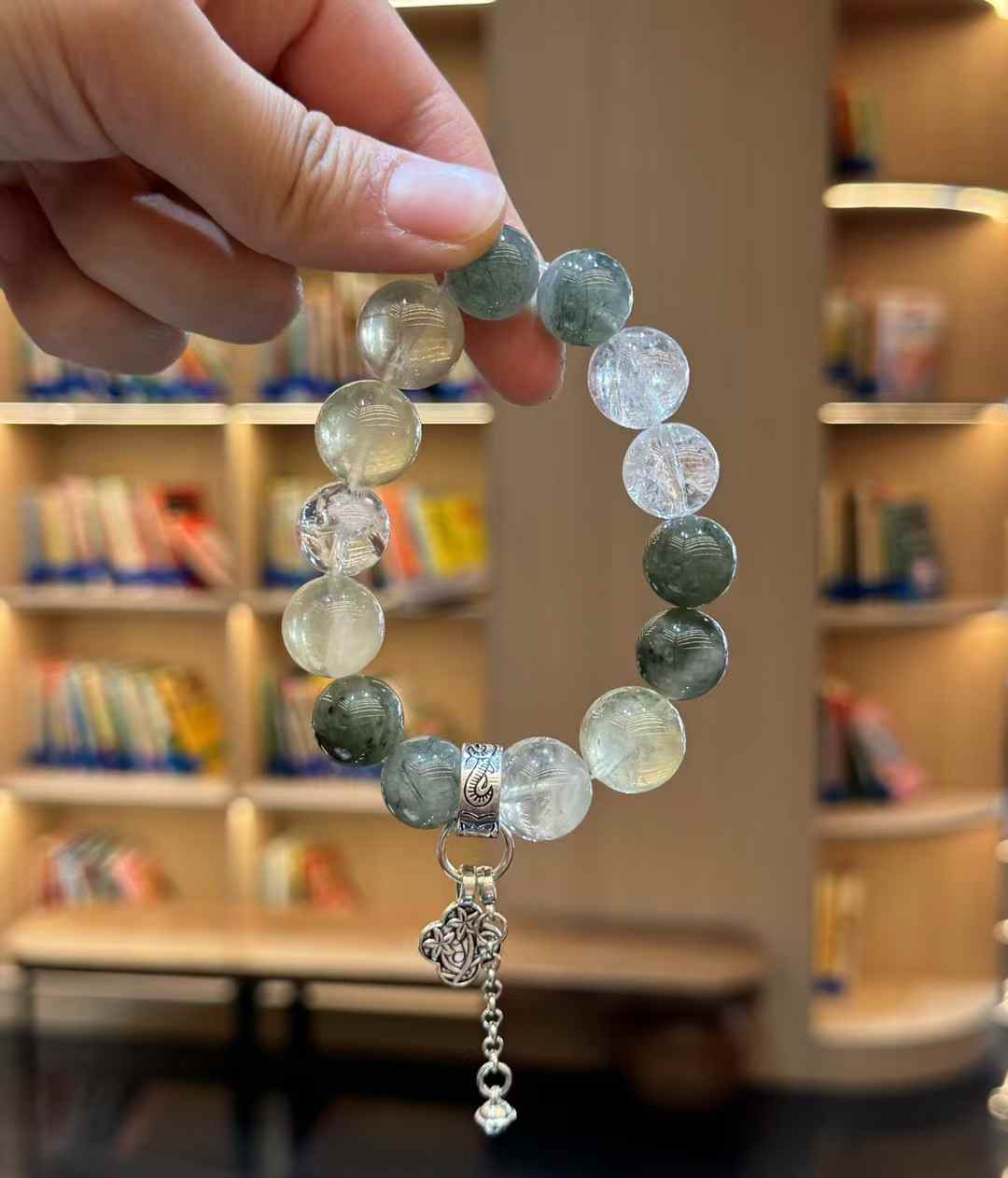 Hanging view of the Green Rutilated Quartz bracelet showing the full circular bead arrangement and dangling charm