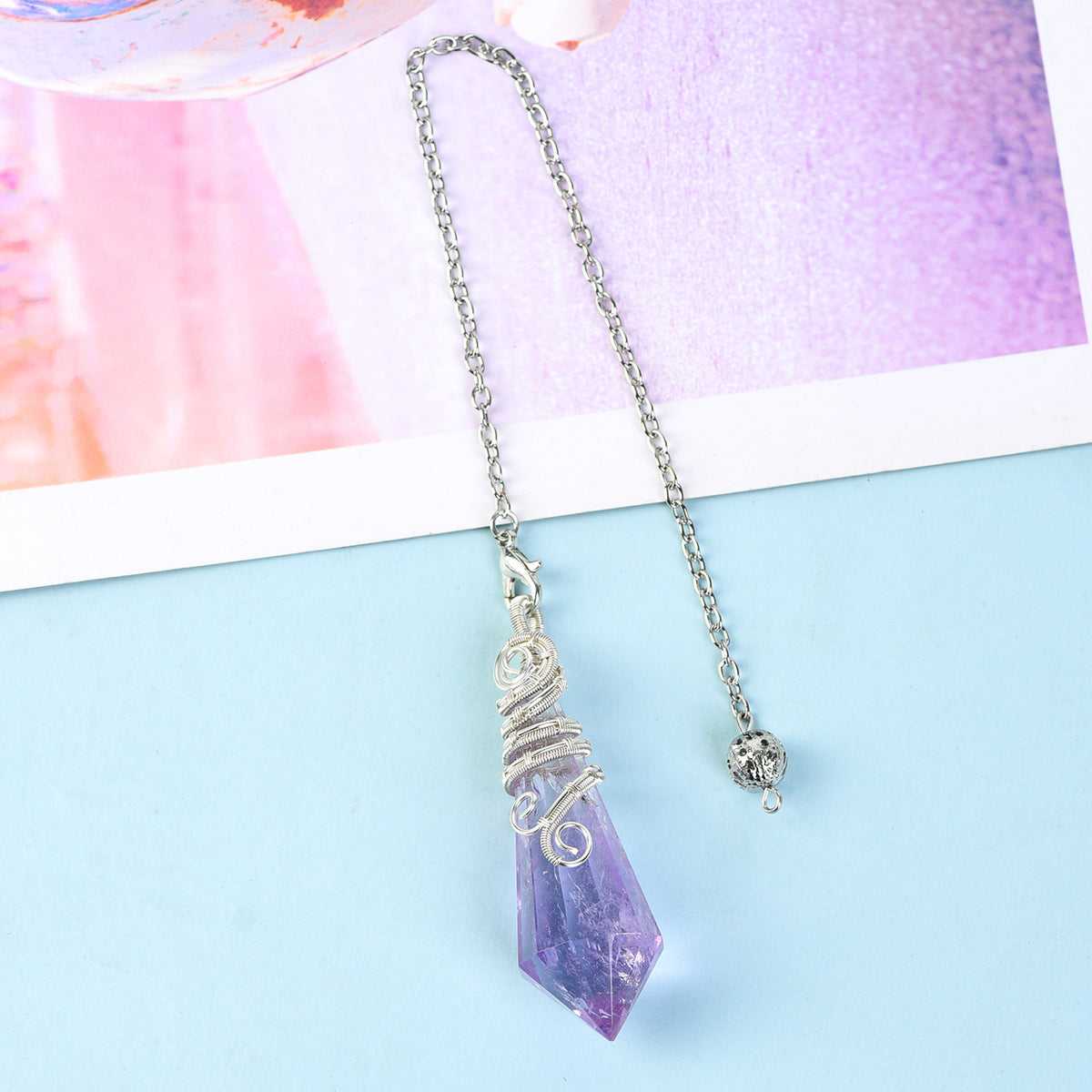 Close-up of a pink faceted crystal pendulum showing the polished geometric point and silver-tone wire detail