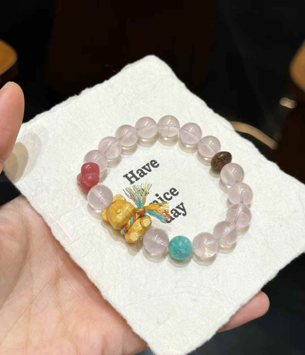 Rose Quartz bead bracelet styled on soft white fabric with wooden bear and butterfly accents