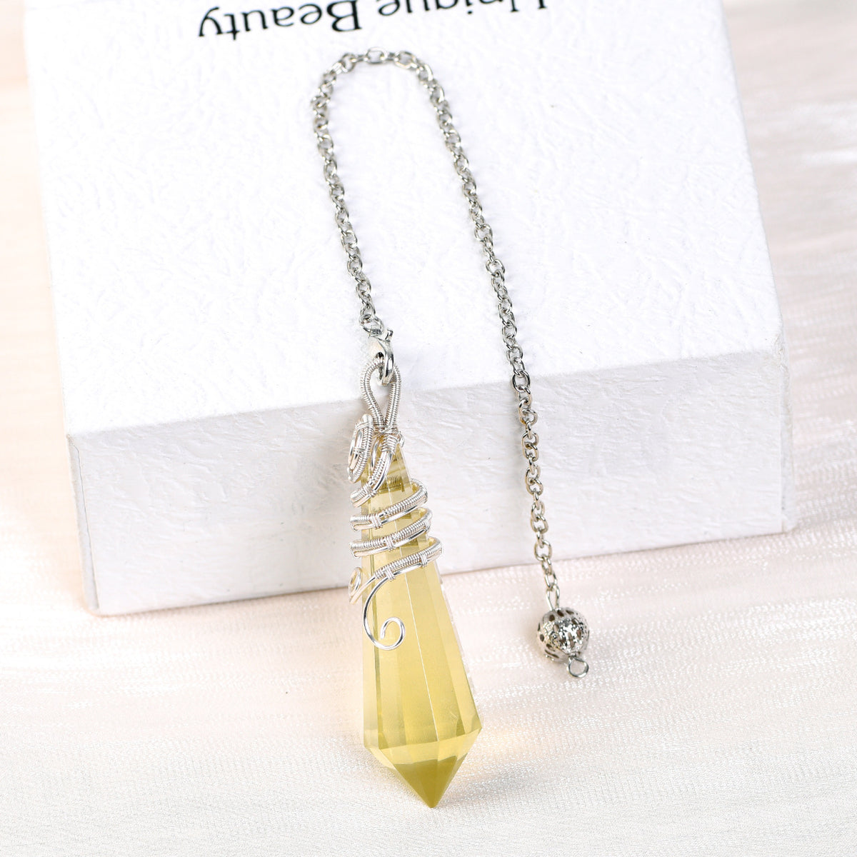 Golden-tone faceted crystal pendulum displayed beside a white box in a clean lifestyle setting