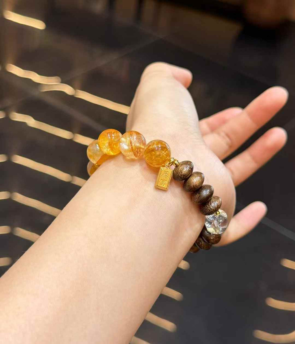 Yellow Hematoid Quartz and Agarwood bracelet worn on the wrist with a small gold-plated copper charm